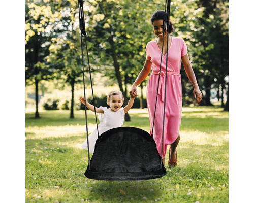Une mère pousse son enfant sur une balançoire dans le jardin.