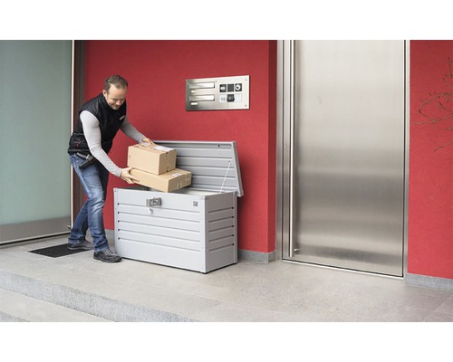 Mann legt Pakete in eine Paketbox vor einem Haus