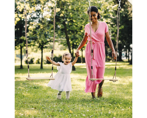 Eine Frau und ein Kind stehen auf einer Wiese neben Schaukeln mit Seilen.