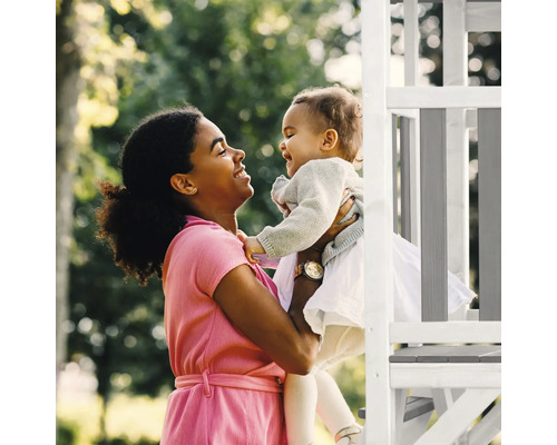 Mutter hebt lachendes Kind vor einem Spielturm hoch