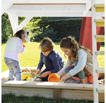 Drei Kinder spielen im Sandkasten unter einem Spielturm im Garten.