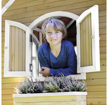 Garçon regardant par la fenêtre d''une cabane de jeu en bois avec jardinière et plantation