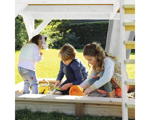 Des enfants jouent dans le bac à sable avec toit et échelle dans le jardin.