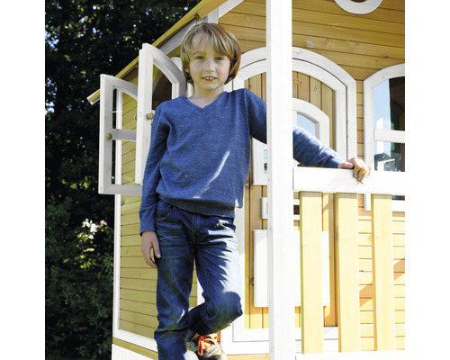 Garçon devant une cabane de jeu en bois avec des fenêtres ouvertes et une balustrade