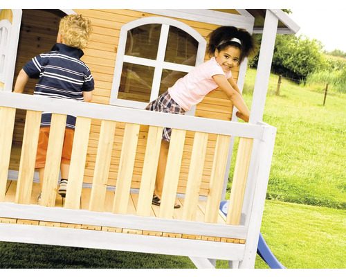 Zwei Kinder spielen in einem Holzspielhaus mit Rutsche im Garten.
