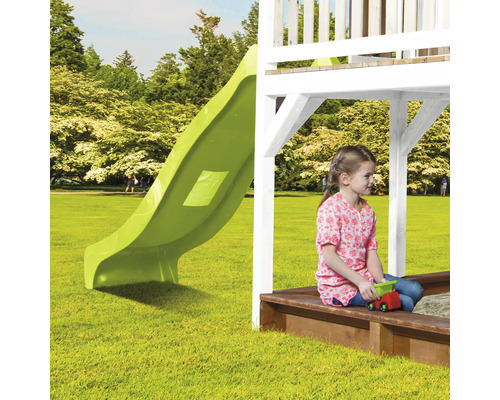 Scène d''une aire de jeux avec toboggan et bac à sable, dans lequel une fille est assise avec une voiture jouet.