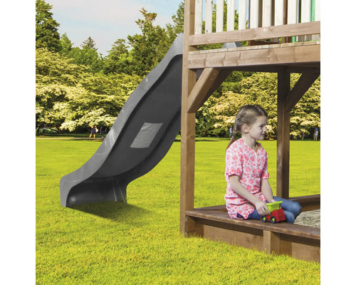 Aire de jeux avec toboggan, bac à sable et enfant jouant dans le jardin.