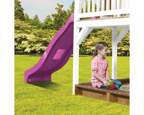 Enfant assis dans un bac à sable sous une tour de jeu avec toboggan