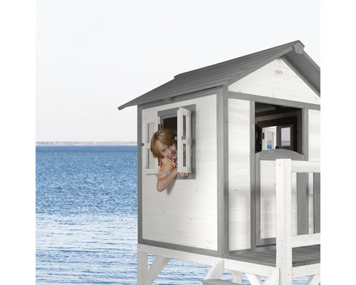 Spielhaus aus Holz mit Fenster und Terrasse, Kind schaut aus dem Fenster.