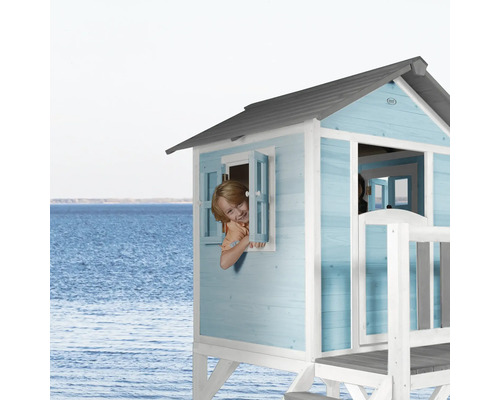 Maisonnette en bois bleue avec enfant à la fenêtre devant un paysage marin