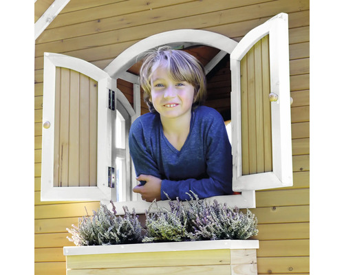 Junge schaut aus dem Fenster eines Holzspielhauses mit Blumenkasten