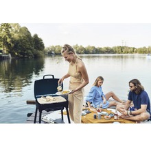 Une personne grille des aliments au bord d''un lac avec un barbecue à gaz Explorer.
