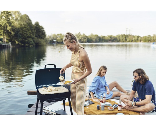 Une personne grille des aliments au bord d''un lac avec un barbecue à gaz Explorer.
