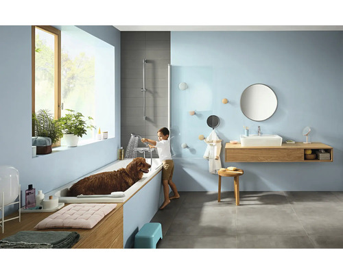 Salle de bains avec baignoire, lavabo, miroir, serviettes et un garçon lavant un chien dans la baignoire.