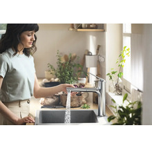 Femme utilisant un robinet de cuisine avec écoulement d''eau dans une cuisine lumineuse.