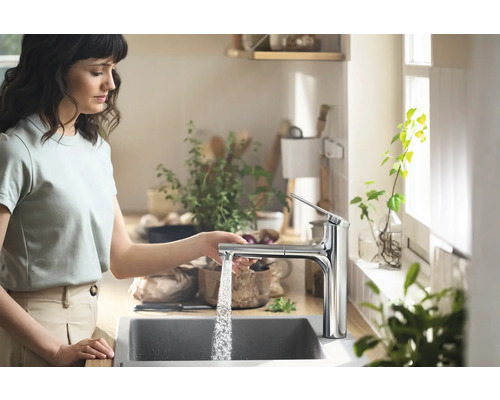 Femme utilisant un robinet de cuisine avec écoulement d''eau dans une cuisine lumineuse.