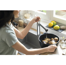 Femme lavant des pommes de terre dans un évier de cuisine sous un robinet.