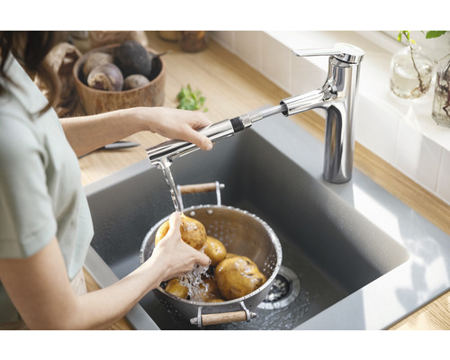 Femme lavant des pommes de terre dans un évier sous un robinet de cuisine avec douchette extractible