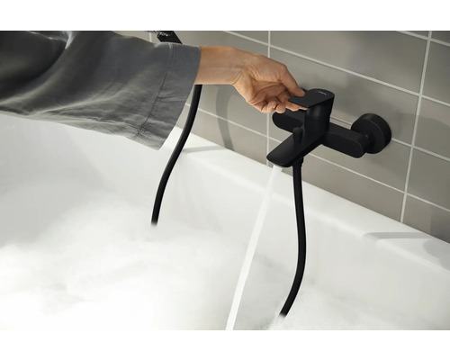 Une personne actionne un robinet de baignoire noir d''où l''eau coule dans une baignoire remplie de mousse.