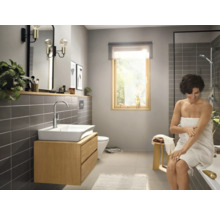 Salle de bain lumineuse avec lavabo, miroir, douche et une femme avec une serviette