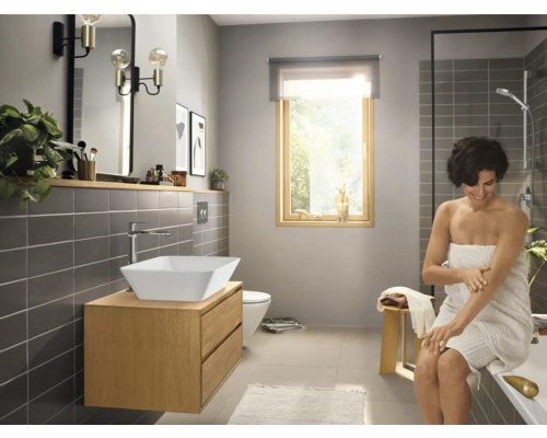 Salle de bains lumineuse avec lavabo, miroir, robinet, toilettes, douche et une femme avec une serviette.
