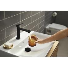 Modernes Badezimmer mit Waschbecken, schwarzer Armatur und einer Person, die ein Glas Wasser füllt.