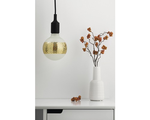 Dekorative Pendelleuchte mit Goldmuster neben einer Vase mit Zweigen auf einem Tisch