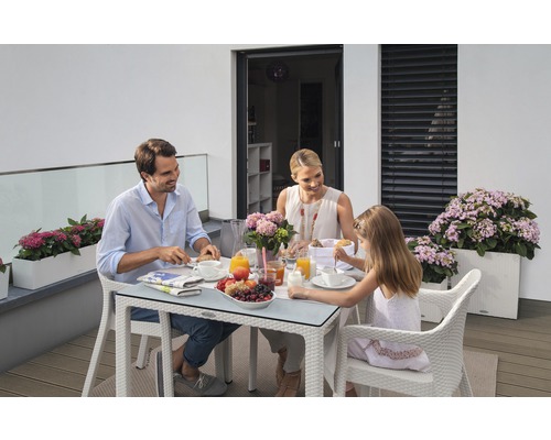 Familie beim Frühstück auf dem Balkon mit Gartentisch und Blumenkästen