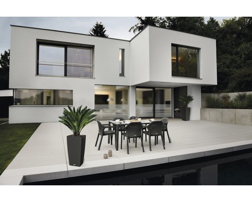 Modernes Haus mit Terrasse, Gartentisch und Stühlen.