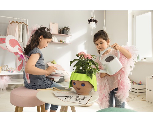Deux filles jouent dans une pièce avec une plante dans un pot avec un visage et un arrosoir.