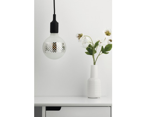 Dekorative Glühbirne mit Schachbrettmuster neben Vase mit Blumen auf einem Tisch