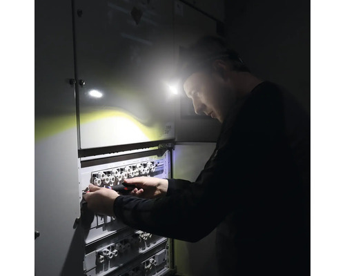 Un homme avec une lampe frontale travaille sur un répartiteur électrique.