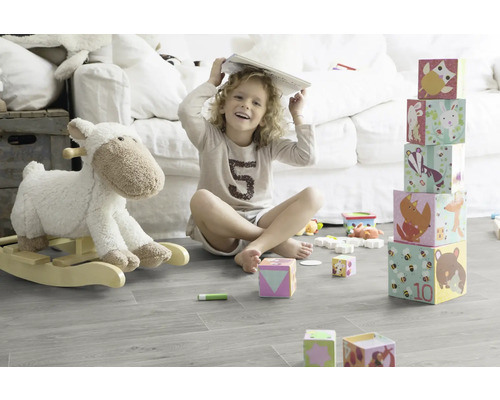 Un enfant est assis avec un livre sur la tête dans une pièce lumineuse et joue avec des blocs de construction et un animal à bascule.