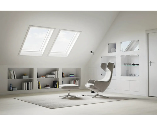 Chambre mansardée lumineuse avec fenêtres de toit, étagères et fauteuil moderne