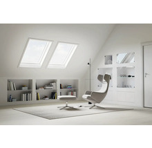 Helles Dachzimmer mit Dachfenstern, Regalen und Sessel mit Fußhocker