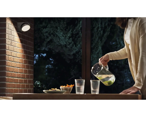 Szene mit einer runden Aussenleuchte an einer Backsteinmauer, während eine Person Getränke einschenkt