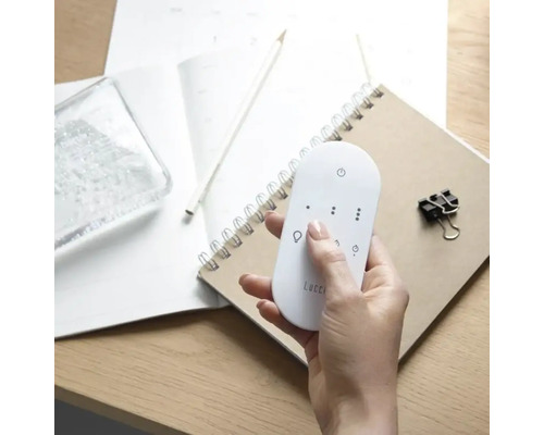 Eine Hand hält eine Lucci Fernbedienung über einem Notizbuch.