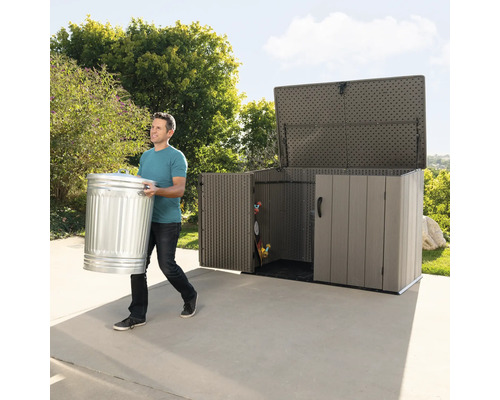 Mann trägt einen Mülleimer zu einer Gerätebox im Garten.