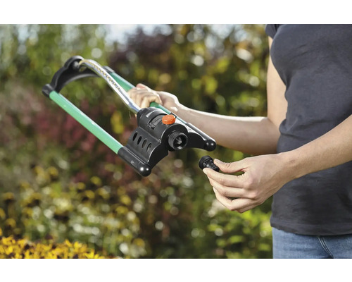 Une femme monte un arroseur de pelouse dans le jardin