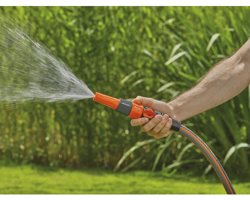 Eine Person hält einen Gartenschlauch mit Sprühdüse, aus der Wasser austritt.