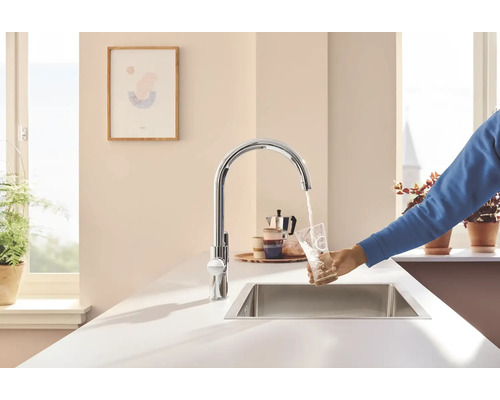 Küchenszene mit Spültischarmatur, Spülbecken und Person, die ein Glas Wasser füllt