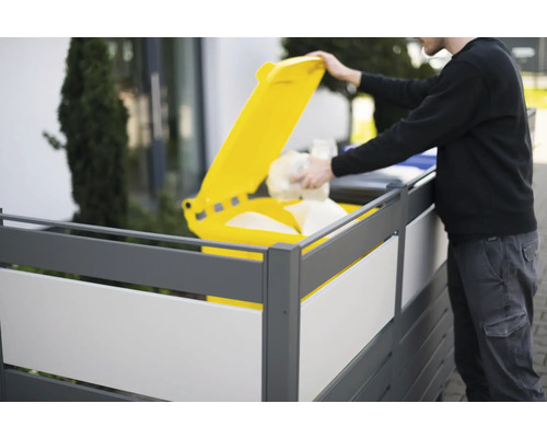 Une personne jette des déchets dans une poubelle jaune derrière un écran d''intimité.