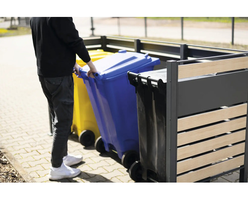 Une personne pousse une poubelle bleue dans un box à poubelles