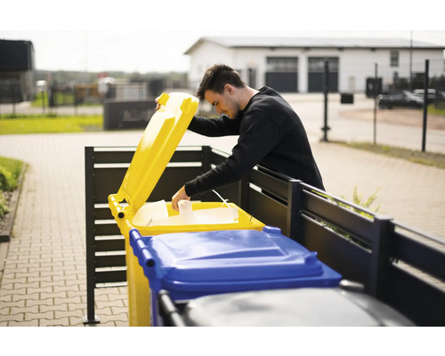 Un homme jette du papier dans une poubelle de recyclage jaune à l''extérieur.