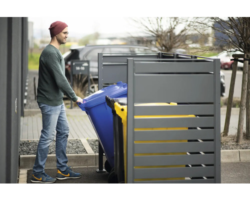 Un homme pousse une poubelle dans un coffre à poubelle