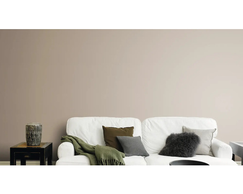 Salon avec canapé blanc, coussins, couverture et vase décoratif sur une table d''appoint devant un mur uni