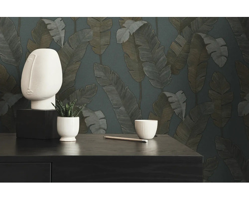 Scène décorative avec une sculpture de tête abstraite, une plante en pot, un crayon et un bol sur fond de papier peint à motifs de feuilles