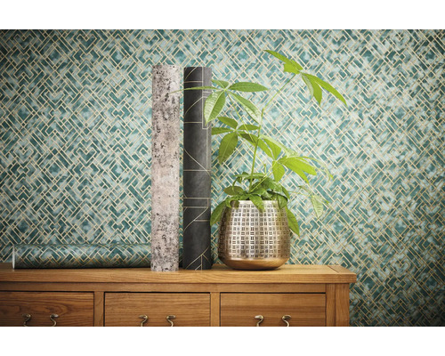 Pièce décorative avec papier peint géométrique, plante et deux rouleaux de papier peint sur une commode en bois