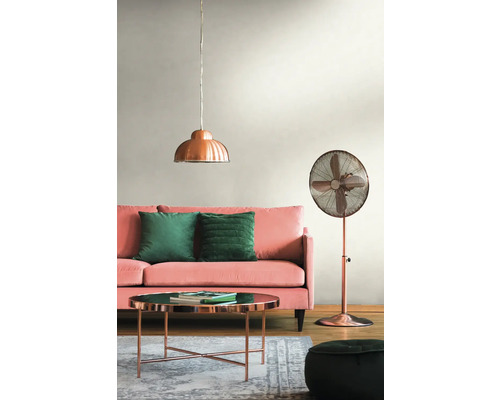 Salon avec canapé rose, coussins verts, table couleur cuivre, lampadaire et suspension.