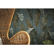 Gros plan d''un fauteuil en osier devant un papier peint à motifs de feuilles.